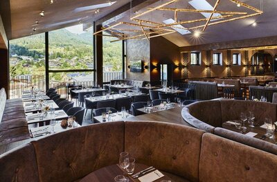Moderner Restaurant-Innenraum mit gepolsterten Sitzbänken, Tischen und großer Fensterfront mit Bergblick.
