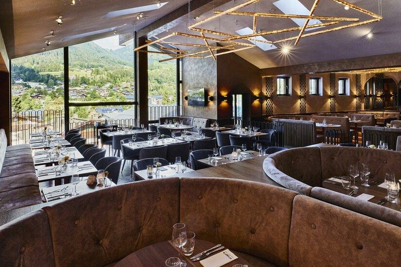 H'ugo's Pizza-Bar-Lounge Moderner Restaurant-Innenraum mit gepolsterten Sitzbänken, Tischen und großer Fensterfront mit Bergblick.