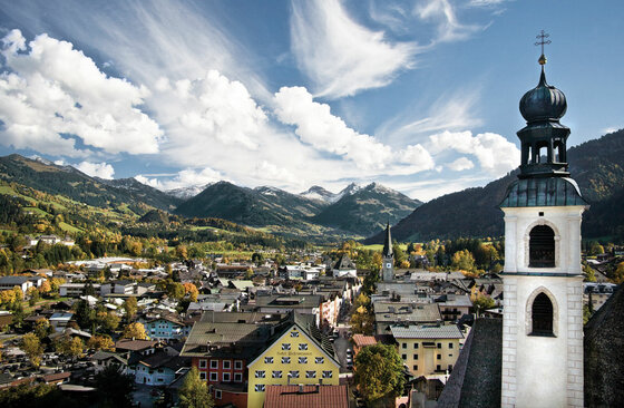 Ortsansicht Kitzbühel Blick über die Dächer von Kitzbühel mit Kirchturm im Vordergrund und Bergen im Hintergrund.