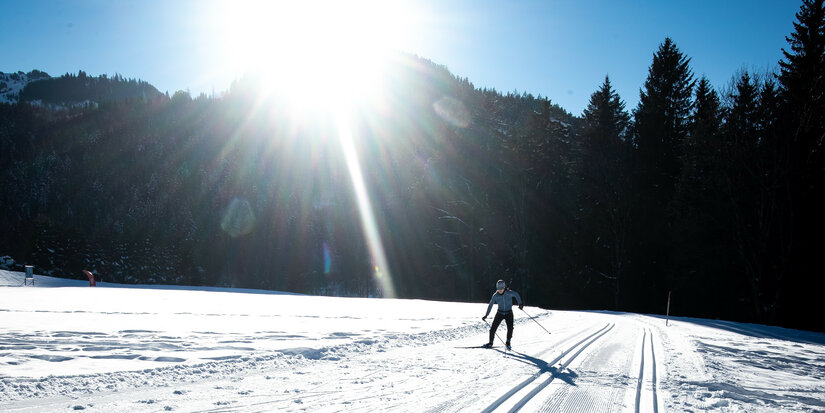 During a cross-country skiing event in Kitzbühel, a skier glides across a snow-covered expanse in bright sunlight.