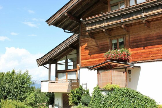 Mehrstöckiges alpines Holzhaus mit Balkonen und Blumenkästen vor blauem Himmel.