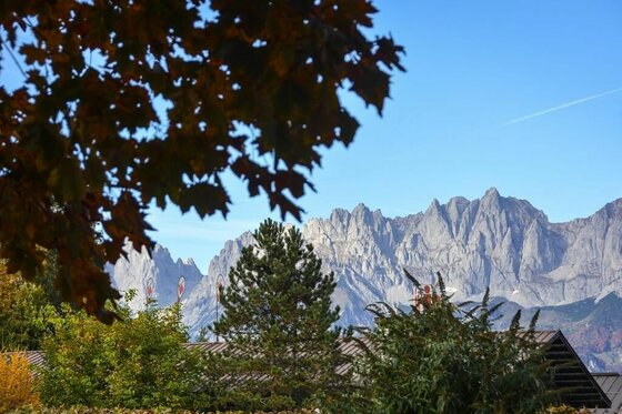 Blick auf das zerklüftete Bergmassiv des Wilden Kaisers hinter Hausdächern und herbstlichen Bäumen.