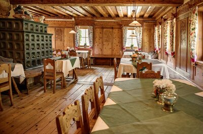 Rustikale Gaststube mit Holztischen, Kachelofen und holzgetäfelten Wänden.