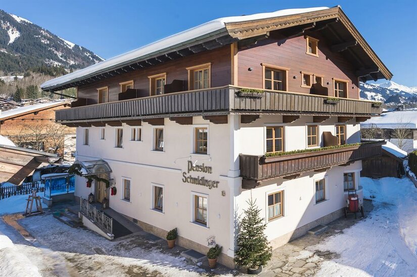 Pension Schmidinger im Winter Mehrstöckiges Gebäude der Pension Schmidinger mit Holzfassade im Obergeschoss und schneebedecktem Dach.