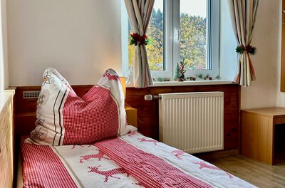 Schlafzimmer im Central Kitz Apartment Einzelbett mit rot-weißer Bettwäsche vor einem Fenster mit Vorhängen.