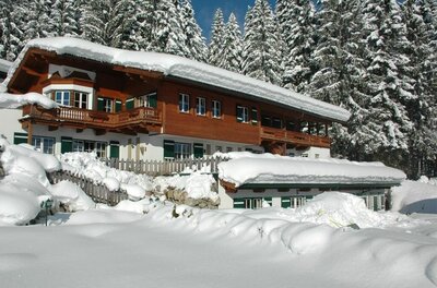Außenansicht Winter Meixner Verschneites Holzhaus mit Balkon vor einem Nadelwald im Winter.