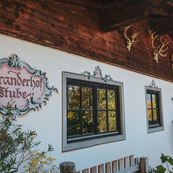 Local Hero Wildpark Aurach (c) Kitzbühel Tourismus Die Fassade eines traditionellen Hauses mit dem Schild 'Branderhof Stube' und kunstvollen Fensterrahmen ist zu sehen.