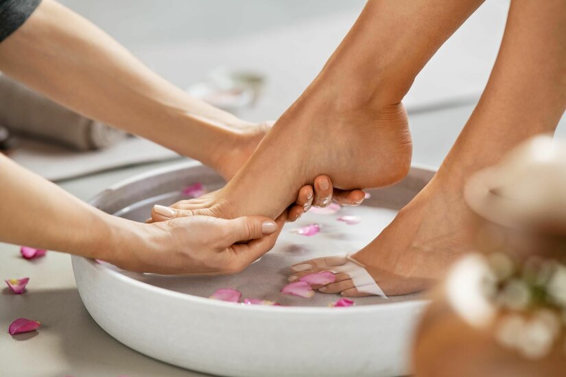 Nahaufnahme einer Fußmassage über einer Schale mit Wasser und Blütenblättern.