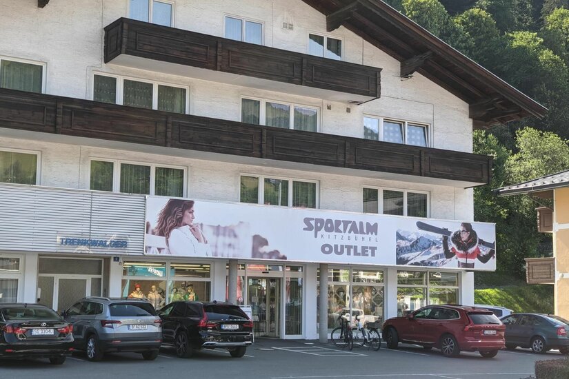Sportalm Outlet Kitzbühel Außenansicht des Sportalm Outlets in einem mehrstöckigen Gebäude mit Parkplatz davor.