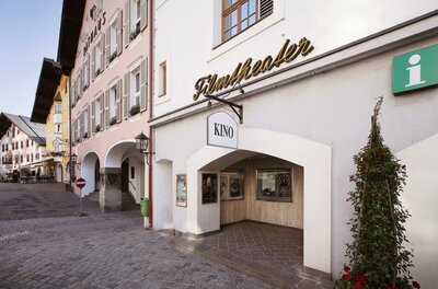 Ein Kino mit dem Namen "Flatholler" in einer malerischen Straße. Die Architektur ist traditionell, umgeben von charmanten Gebäuden und Pflanzen.