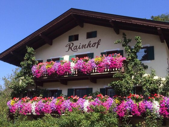 Blumenschmuck am Rainhof Fassade des Rainhofs mit zwei Holzbalkonen, die dicht mit pinken und violetten Blumen bewachsen sind.