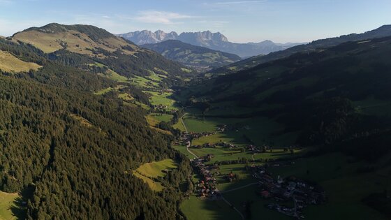 Blick ins Spertental Luftaufnahme eines grünen Alpentals mit bewaldeten Hängen, kleinen Siedlungen und schroffen Berggipfeln im Hintergrund.
