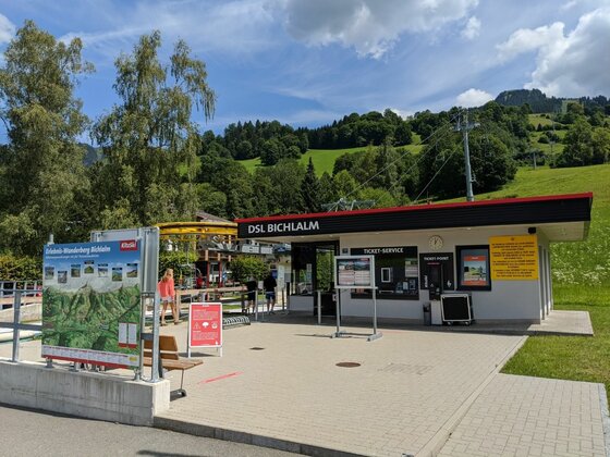 Talstation Bichlalmlift Talstation der DSL Bichlalm mit Ticket-Service, Informationstafeln und bewaldetem Hang im Hintergrund.