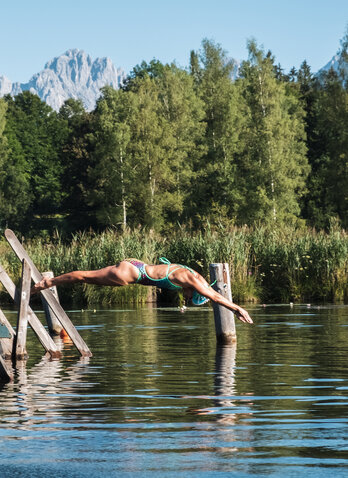 Lake Schwarzsee in Kitzbühel and a woman diving headfirst into it from the jetty