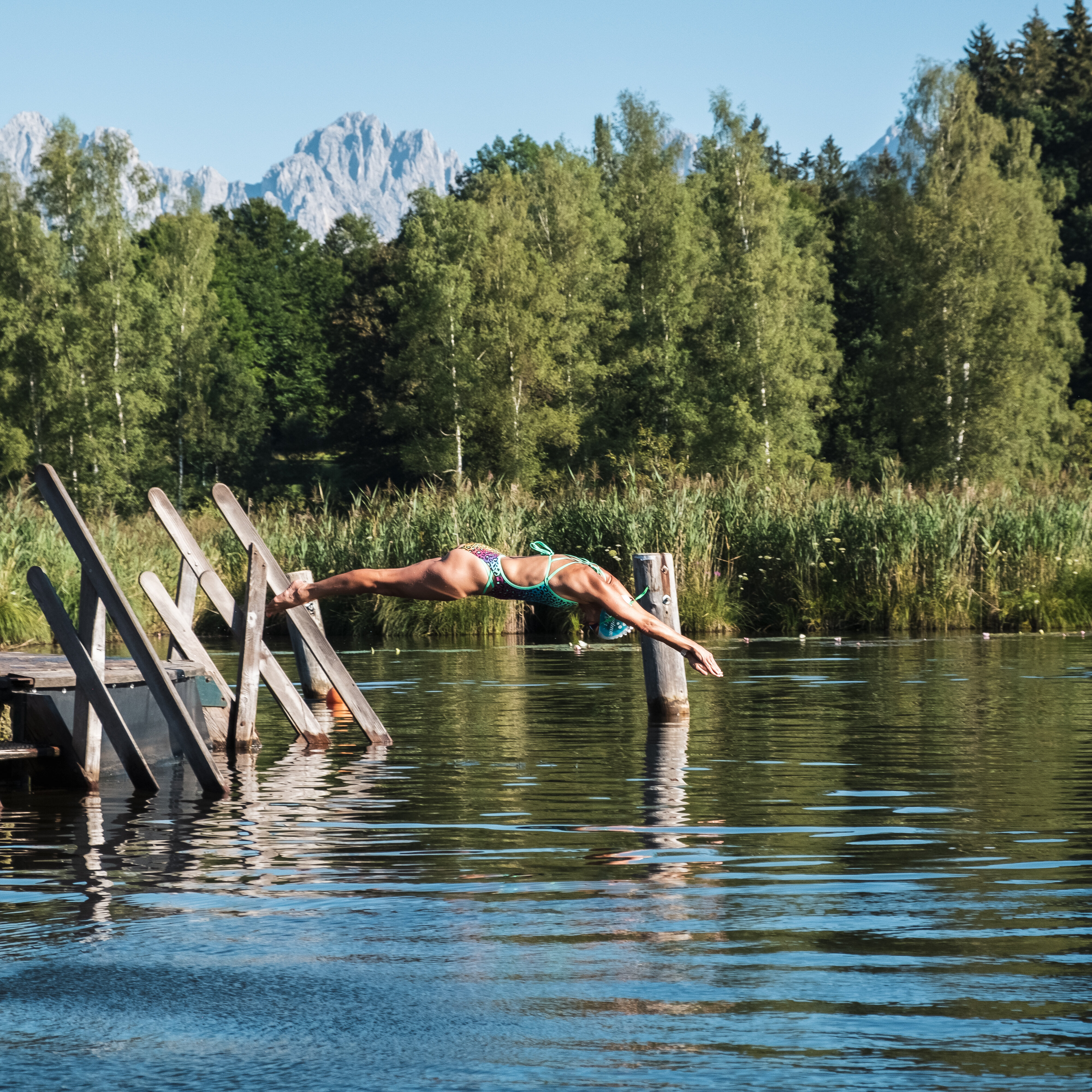 Der Schwarzsee in Kitzbühel und eine Frau, die einen Kopfsprung vom Steg aus hinein macht