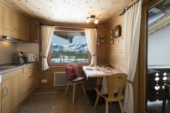 Landhaus Klotz Apartment Jimmy Küche Kleine Holzküche mit Esstisch und Fenster mit Blick auf verschneite Berge.