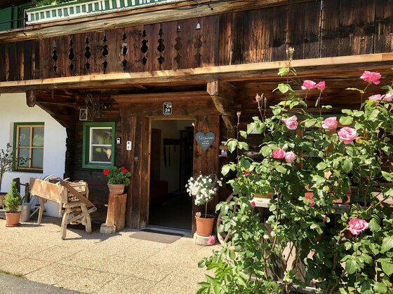 Eingang MyApart 1709 Eingangsbereich eines traditionellen Holzhauses mit Blumen und einem Balkon aus dunklem Holz.