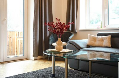 605345670 Ein heller Wohnraum mit einem grauen Sofa und einem Couchtisch. Auf dem Tisch steht eine Vase mit roten Blumen.