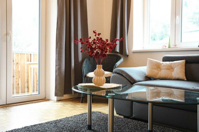605345670 Ein heller Wohnraum mit einem grauen Sofa und einem Couchtisch. Auf dem Tisch steht eine Vase mit roten Blumen.