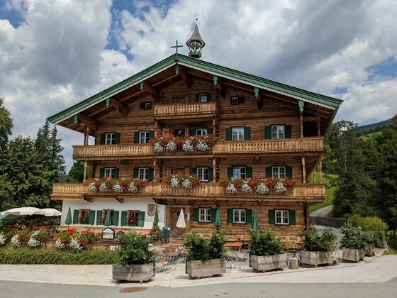 Alpiner Gasthof in Aurach Mehrstöckiges Holzhaus im alpinen Stil mit Blumenschmuck an den Balkonen und einer Außenterrasse.