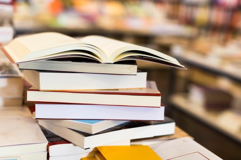 Ein Stapel verschiedener Bücher mit einem aufgeschlagenen Buch obenauf in einer Bücherei.