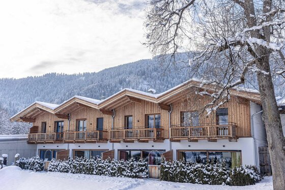Chalet Streif Dorfresort Kitzbühel Zweistöckiges Holzchalet mit Balkonen in einer verschneiten Winterlandschaft vor bewaldeten Bergen.