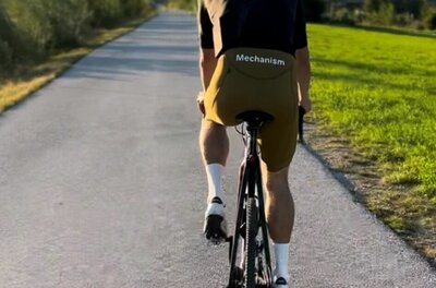 Ein Rennradfahrer von hinten auf einem asphaltierten Weg vor einer Bergkulisse.