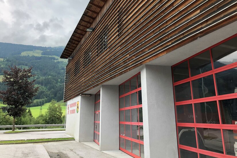 Feuerwehr Jochberg <p>Das Feuerwehrgebäude von Jochberg mit Holzverkleidung und großen Fenstern. Im Hintergrund sind grüne Wiesen und Berge zu sehen.</p>