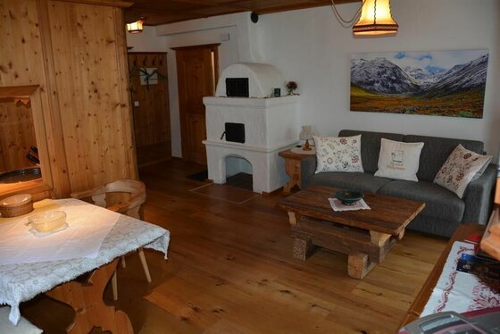 Rustikaler Wohnraum mit Holzboden, weißem Kachelofen, grauem Sofa und massivem Couchtisch.
