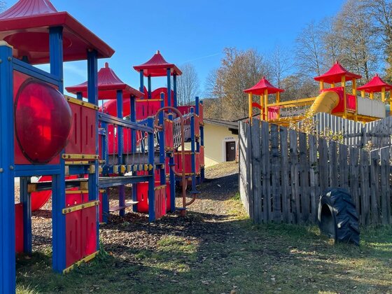 Bunter Kinderspielplatz mit Klettergerüsten, Rutschen und Holzzaun unter blauem Himmel.