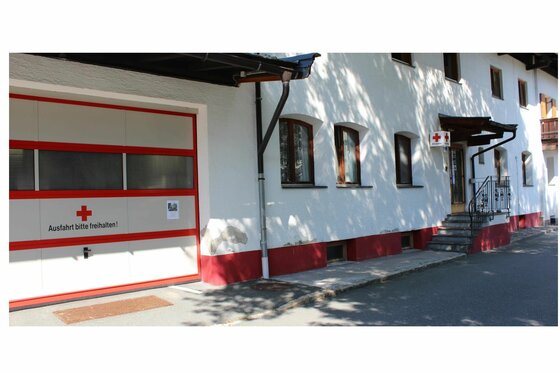 Weißes Gebäude mit Garagentor des Roten Kreuzes und Treppenaufgang.