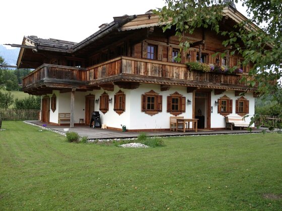Chalet Nestwärme Außenansicht Zweistöckiges Holzchalet mit weißem Erdgeschoss, Holzbalkon und grüner Rasenfläche.