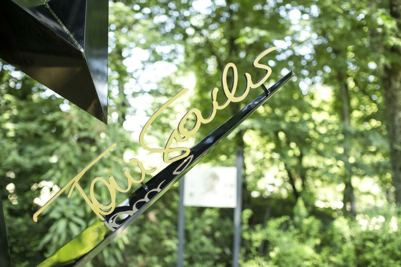 Legendenpark Ein elegantes Schild mit der Schrift "Tourists" in goldener Farbe, das vor einer grünen, bewaldeten Kulisse steht. Der ruhige Hintergrund sorgt für eine angenehme Atmosphäre.