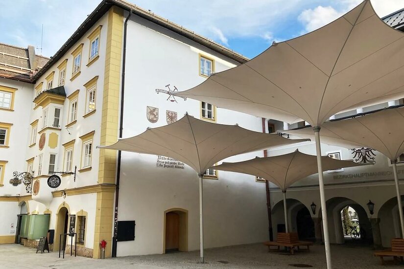 Innenhof eines historischen Gebäudes mit großen weißen Sonnenschirmen und gelben Fassadendetails.