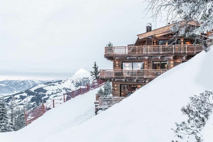 Hahnenkamm Lodge Kitzbühel Mehrstöckiges Holzchalet an einem verschneiten Berghang mit Blick auf die Alpen.