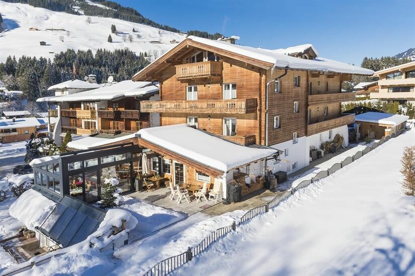 Mehrstöckiges Holzhaus mit schneebedecktem Dach und Terrasse in einer winterlichen Berglandschaft.