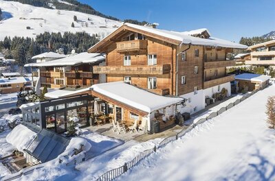 Haus Winter Hotel-Pension Mehrstöckiges Holzhaus mit schneebedecktem Dach und Terrasse in einer winterlichen Berglandschaft.