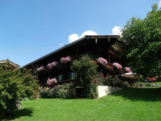 Haus Ansicht Sommer Traditionelles Holzhaus mit blumengeschmückten Balkonen und grünem Garten unter blauem Himmel.