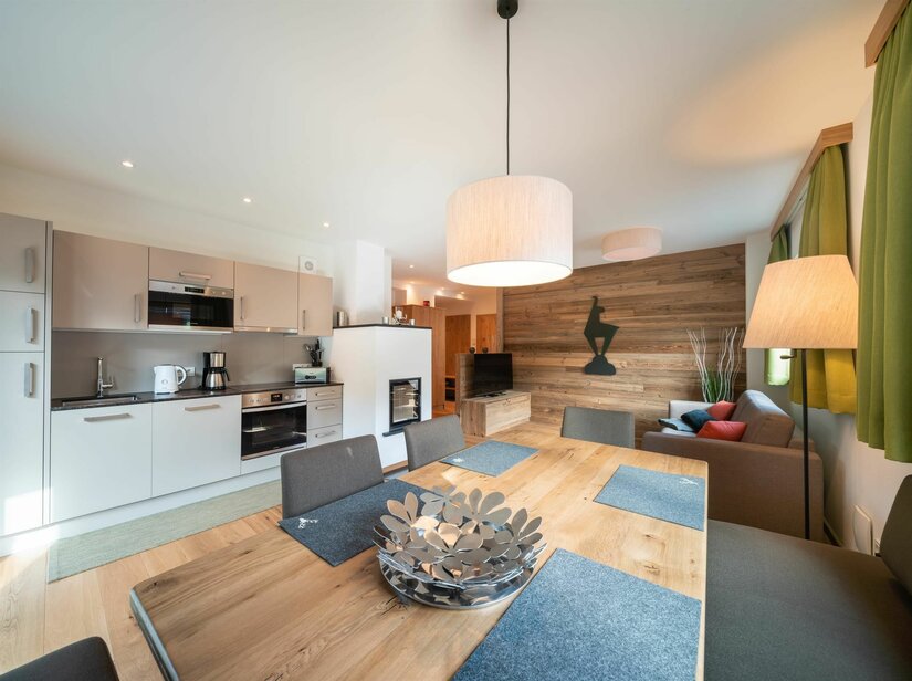 Wagstätt Residenz Jochberg Moderner Wohn- und Essbereich mit Holztisch, Küchenzeile und Sofa vor einer Holzwand.