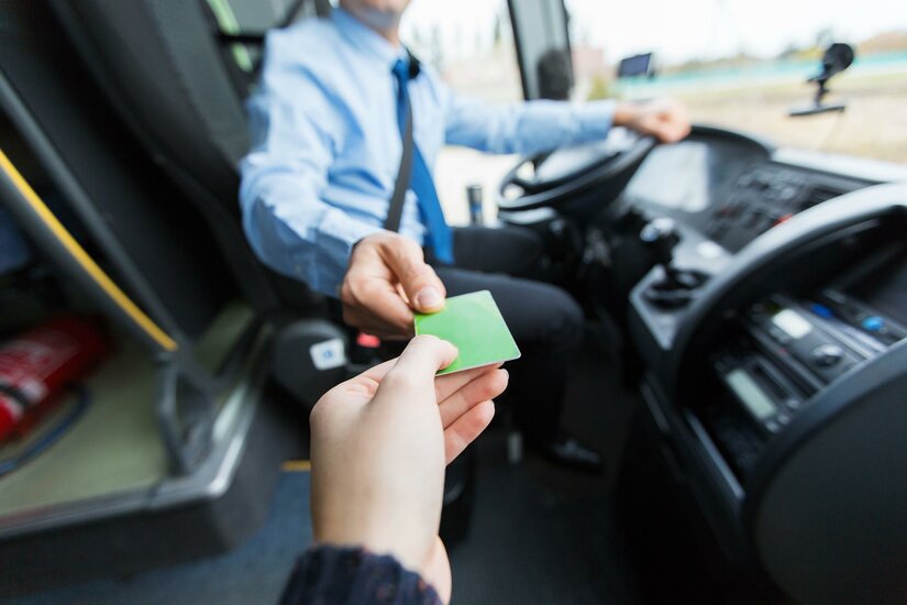 Entstrasser Ein Fahrgast gibt dem Busfahrer eine grüne Fahrkarte. Der Fahrer sitzt am Steuer des Busses.
