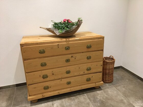 Eingangsbereich Bauernhof Froidl Rustikale Holzkommode mit Blumenschale und Flechtkorb in einem hellen Raum.