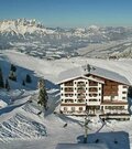 Großes Hotelgebäude in einem verschneiten Skigebiet vor einem weiten Bergpanorama.