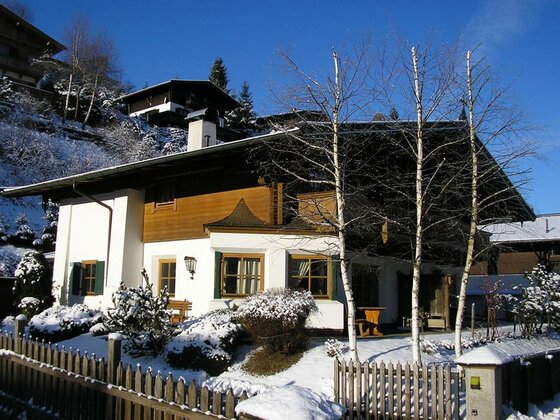 Außenansicht Haus Staudach Alpines Wohnhaus mit weißer Fassade und Holzgiebel in verschneiter Landschaft unter blauem Himmel.