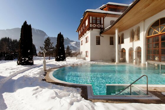 MOMENTUM SPA im Winter Außenpool eines Hotels in verschneiter Landschaft mit Bergen im Hintergrund.