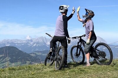 Mountainbiker am Gipfel Zwei Mountainbiker geben sich auf einem Berggipfel vor einem Alpenpanorama ein High-Five.
