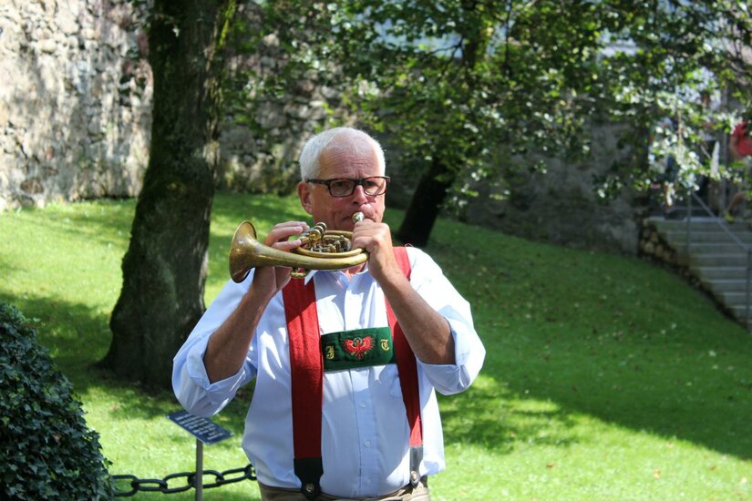 Kitz Events Ein älterer Mann spielt ein Instrument in einem grünen Park. Er trägt eine traditionelle Tracht mit Hosenträgern.