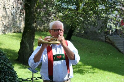 Kitz Events Ein älterer Mann spielt ein Instrument in einem grünen Park. Er trägt eine traditionelle Tracht mit Hosenträgern.