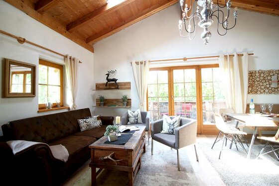 Wohnzimmer OG Chalet Belle Kitz Wohnzimmer mit braunem Sofa, zwei grauen Sesseln, Holztisch und Blick auf einen Balkon.