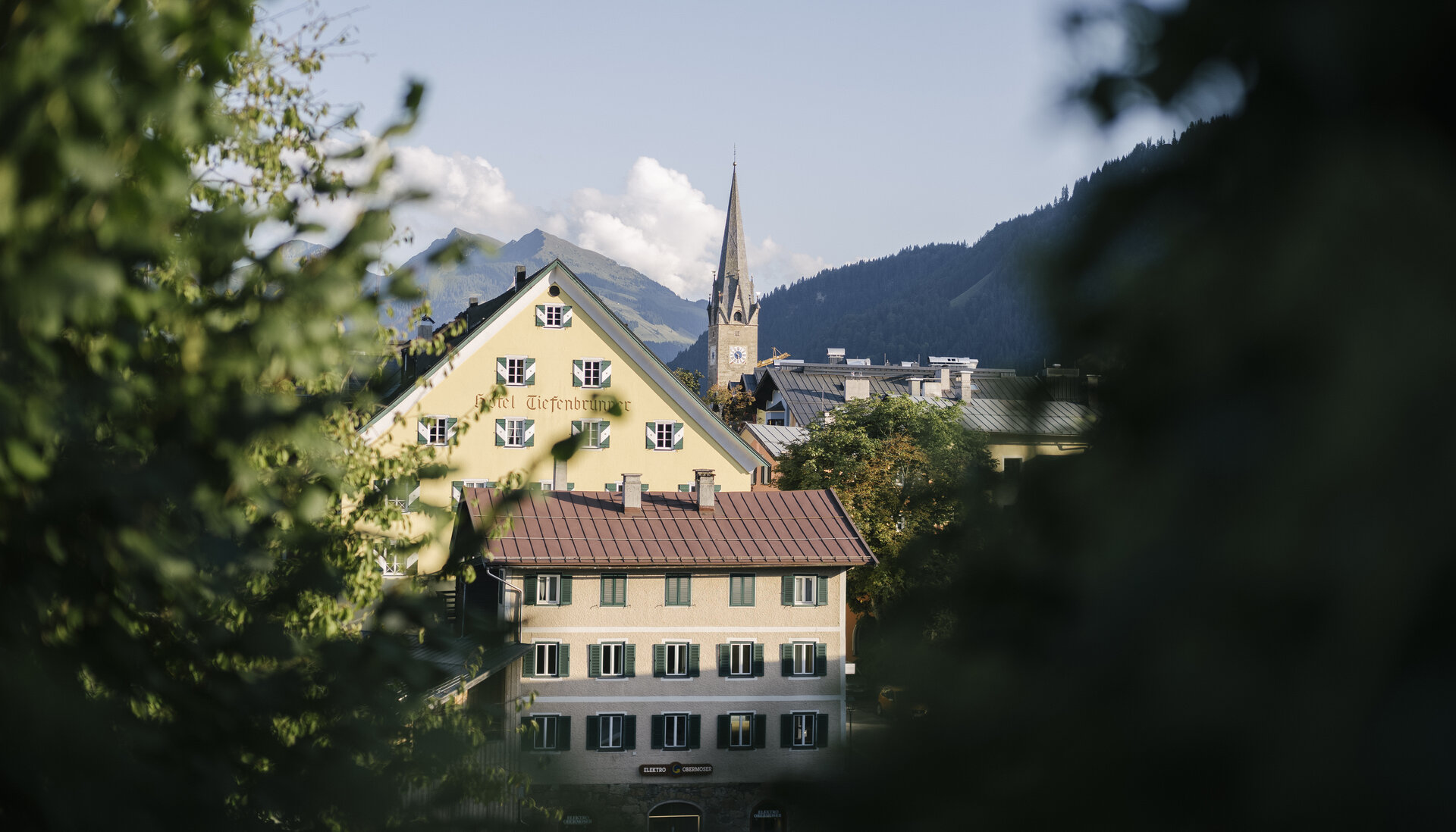 Kitzbühel mit bunten Häusern und Kirche, umgeben von Bergen und klarem Himmel.