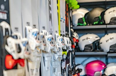 Mehrere Paar Ski in einer Halterung und Skihelme in einem Regal.